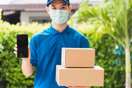 Asian delivery express courier young man giving boxes to customer he wears protective face mask at front home and show mobile phone blank screen, under curfew quarantine pandemic coronavirus COVID-19