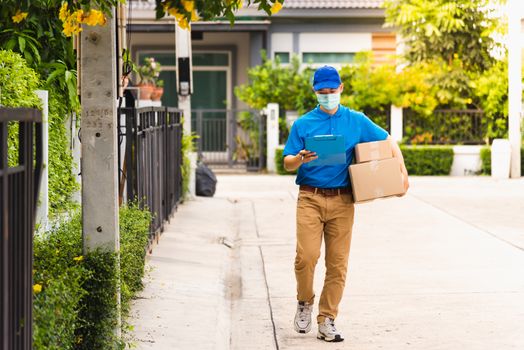 Asian young delivery man courier hold parcel post boxes he protective face mask service and walk looking for customer home location, under curfew pandemic coronavirus COVID-19