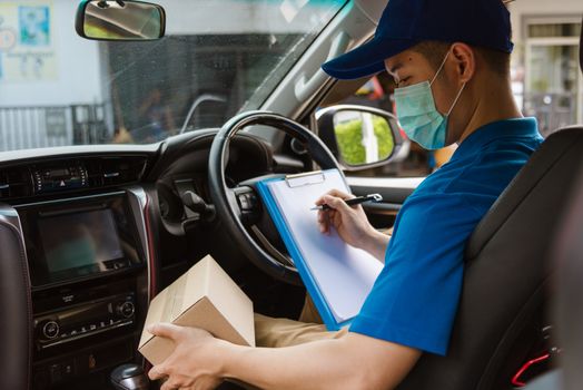 Asian delivery courier young man driver inside the van car with parcel post boxes checking amount he protective face mask, under curfew quarantine pandemic coronavirus COVID-19