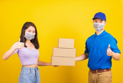 Asian beautiful woman and handsome man wearing protection face mask against coronavirus, accepting delivery boxes, studio shot isolated on yellow background, COVID-19 or corona virus concept