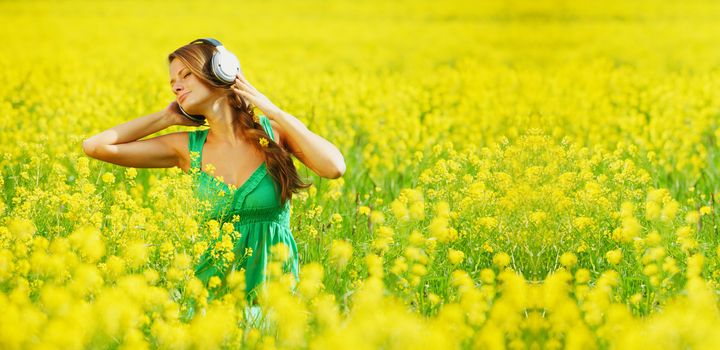 Young woman with headphones listening to music on oilseed flower field