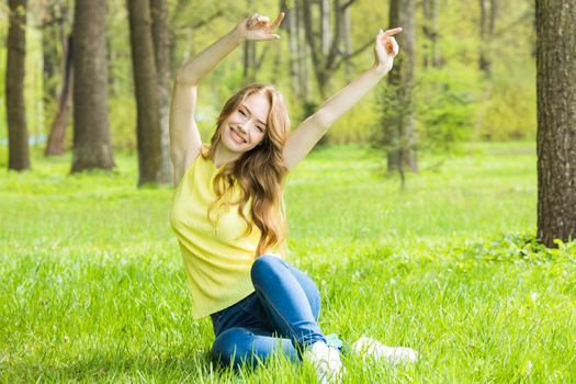 Young attractive woman relaxing in nature , stretching raised arms sitting in park on spring grass