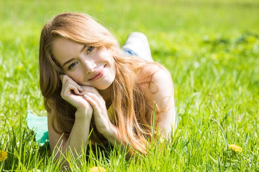 Happy smiling young woman laying on the green grass