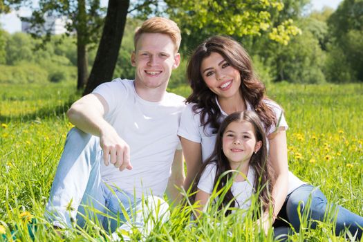 Family of three sitting on spring park meadow grass being happy