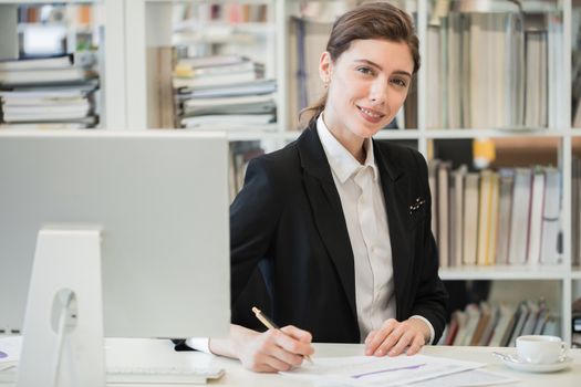 Young female business woman sitting at her workplace with computer monitor and working with financial reports