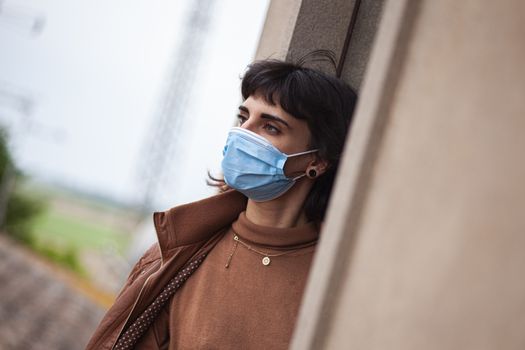 Girl with medical mask at window in her home during covid quarantine period