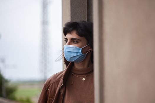 Girl with medical mask at window in her home during covid quarantine period