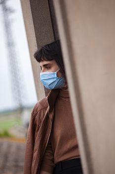 Girl with medical mask at window in her home during covid quarantine period