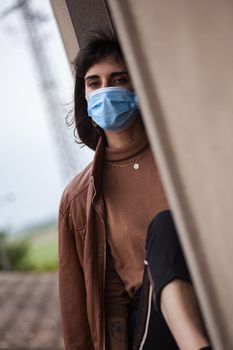 Girl with medical mask at window in her home during covid quarantine period