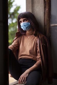 Girl with medical mask at window in her home during covid quarantine period