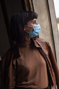 Girl with medical mask at window in her home during covid quarantine period