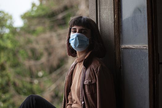 Girl with medical mask at window in her home during covid quarantine period