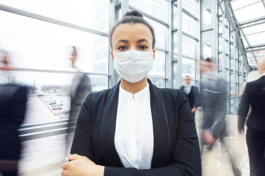 Beautiful african business woman in suit wearing surgical protect mask standing in a crowd of walking people. Concept for prevent for coronavirus outbreak