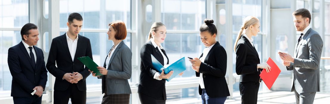 Corporate business team, people standing by the window at break and talking discussing documents