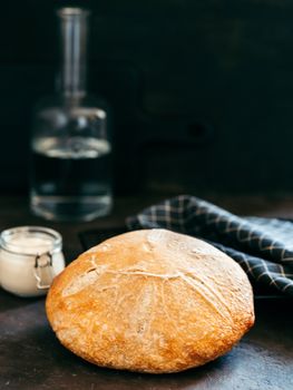 Wheat round sourdough bread and sourdoug starter in glass jar. Side view of delicious homemade sourdough bread on black background with copy space. Home made sourdough bread making concept. Vertical.