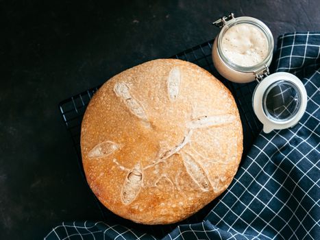 Wheat round sourdough bread and sourdoug starter in glass jar. Top view of delicious homemade sourdough bread on black background with copy space. Home made sourdough bread making concept.