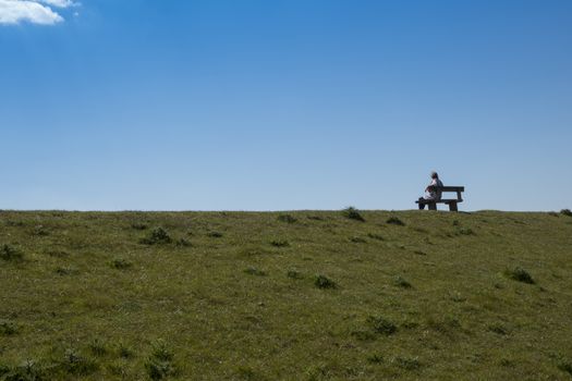 adult woman sits on a bench enjoying nature with blue sky and green grassalleen