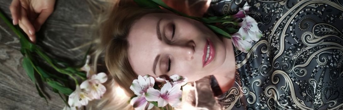 Portrait of a beautiful fashionable middle-aged woman with long blond hair, lying among white flowers and a garland of lights.