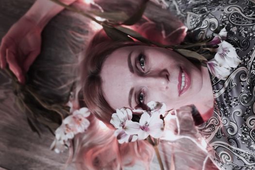 Portrait of a beautiful fashionable middle-aged woman with long blond hair, lying among white flowers and a garland of lights.