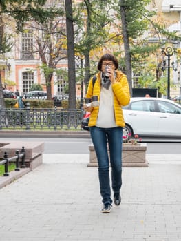 Take away coffee. Women in bright yellow jacket holds paper cup with freshly brewed cappuccino. Hot beverage on cool autumn day.