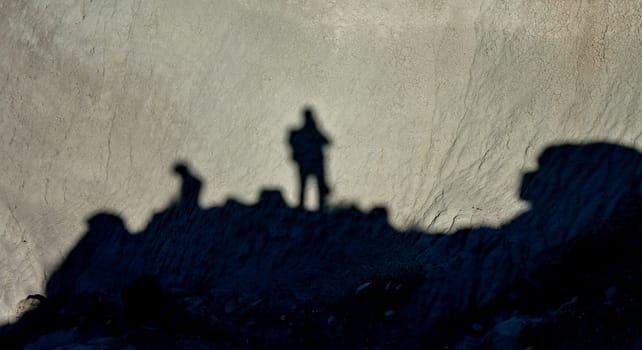 Shadow of a man against a background of dry cracked clay, cracks on the ground.
