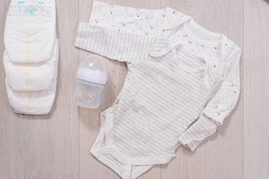 white baby clothes, diapers and baby milk bottle wooden background. newborn