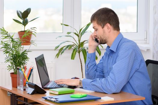 The specialist in the office works at the computer and talks on the phone