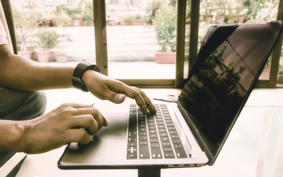 Side view shot of hands of a busy business man working in notebook laptop doing project on office desk. Businessman using computer on wooden table. Close-up. Vintage style. Copy space room for text.