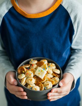 Trendy food - pancake cereal. Heap of mini cereal pancakes in boul in kids hands. Unrecognizable child hold gray bowl with tiny pancakes decorated sprinkles and butter. Copy space. Vertical.