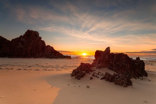 Golden sunrise over the ocean horizon spreading warm light onto a remote rocky beach