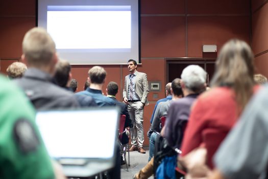 Speaker giving a talk in conference hall at business meeting event. Rear view of unrecognizable people in audience at the conference hall. Business and entrepreneurship concept.