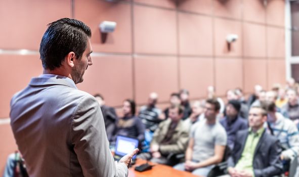 Speaker giving a talk on corporate business conference. Unrecognizable people in audience at conference hall. Business and Entrepreneurship event.