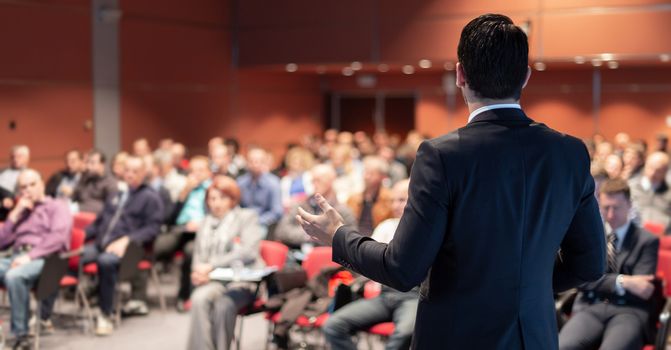 Speaker giving a talk on corporate business conference. Unrecognizable people in audience at conference hall. Business and Entrepreneurship event.