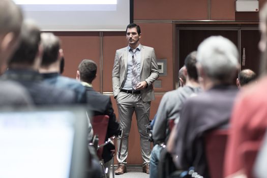 Speaker giving a talk in conference hall at business meeting event. Rear view of unrecognizable people in audience at the conference hall. Business and entrepreneurship concept.