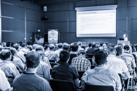 Female speaker giving presentation in lecture hall at university workshop. Audience in conference hall. Rear view of unrecognized participant in audience. Scientific conference event.