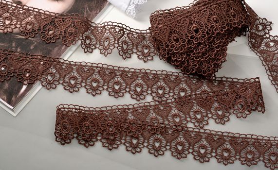 Tapes of brown gentle guipure, beauty lace fabric on light background. Elastic material. Using for Atelier and needlework store.