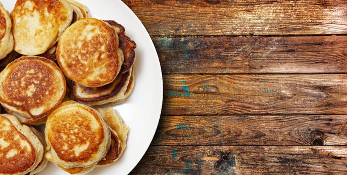 A pile of freshly baked pancakes lay on a plate isolated on wooden table background. Top view. With clipping path.