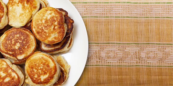 CHISINAU, MOLDOVA - May 18, 2020: Pile of freshly baked pancakes lay on a white plate on a folk embroidery fabric handmade close up. Top view