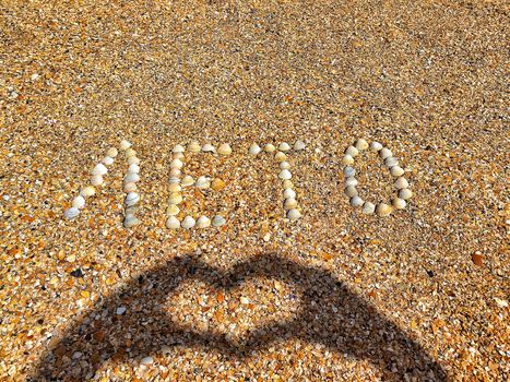 The word summer is lined with scallops shells on the coastal sand. A shadow from the heart-shaped hands. I love summer.