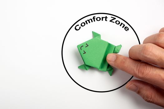 Step out from the comfort zone concept. A dark green origami frog is ready to jump out of the comfort zone.