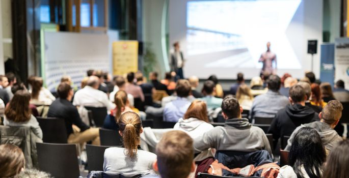 Speaker giving a talk in conference hall at business event. Rear view of unrecognizable people in audience at the conference hall. Business and entrepreneurship concept.