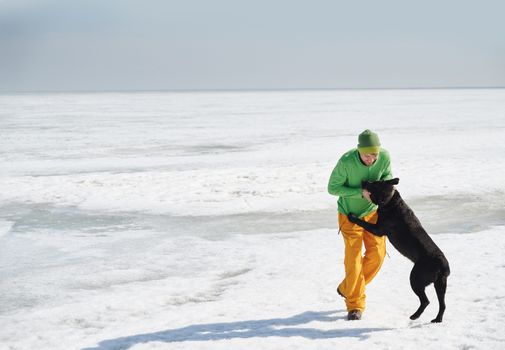 Young adult man outdoors with his dog having fun in winter landscape
