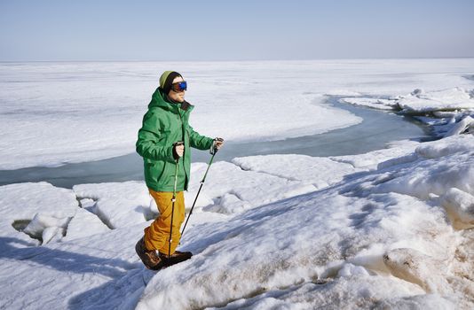 Young adult man with walking sticks outdoors exploring icy landscape