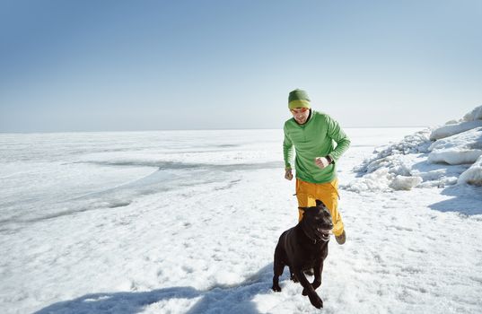 Young adult man outdoors with his dog having fun in winter landscape