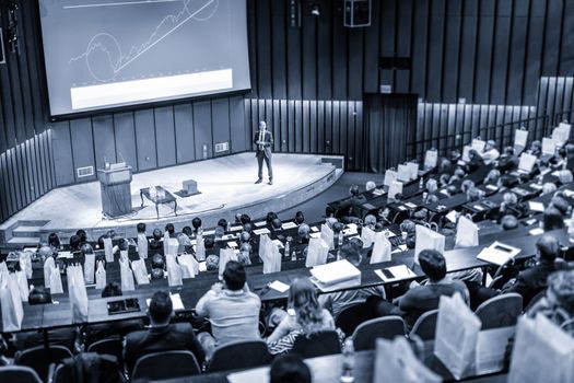 Speaker Giving a Talk at Business Meeting. Audience in the conference hall. Business and Entrepreneurship concept. Blue toned.