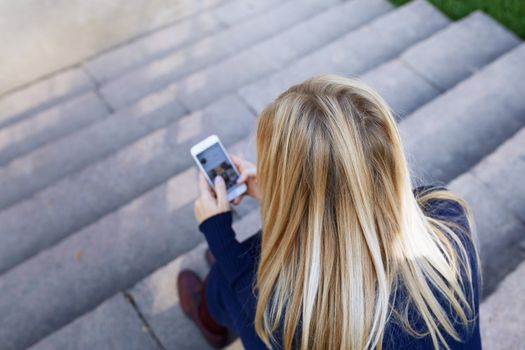 Business woman sitting on city stair steps and holding smartphone
