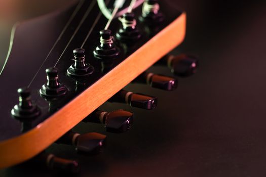 Closeup tuning key on the headstock of the black electric guitar in dark background and morning light. Copy space on the right. Concept of good memory About retro musical instruments and rock music.