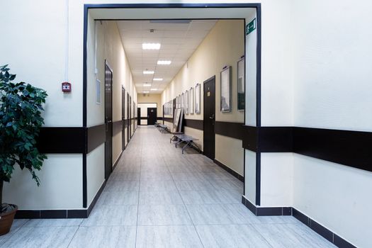 empty corridor in the modern office building. There are many brown doors along a very long corridor with beige walls.