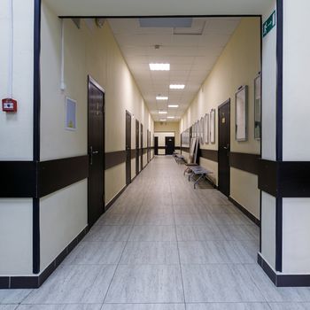 empty corridor in the modern office building. There are many brown doors along a very long corridor with beige walls.