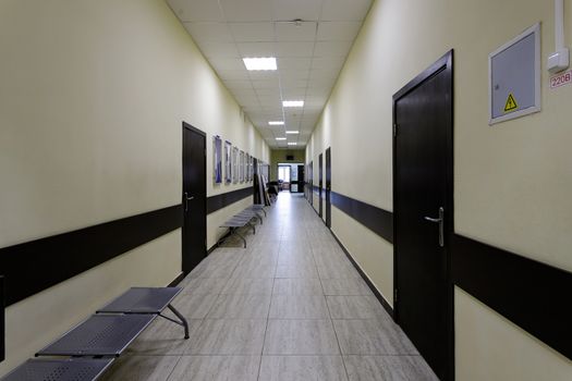 empty corridor in the modern office building. There are many brown doors along a very long corridor with beige walls.